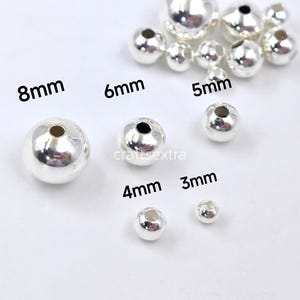 May include: A collection of round, metallic silver-colored beads in various sizes, labeled with text indicating diameters of 3mm, 4mm, 5mm, 6mm, and 8mm. The beads feature a smooth, reflective surface and a central hole for threading, arranged in a group.