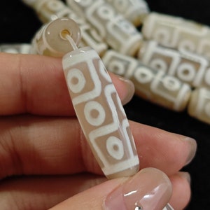 Puede incluir: Primer plano de un collar de cuentas de ágata blanca con un patrón geométrico. Las cuentas son cilíndricas y tienen un acabado liso y pulido.