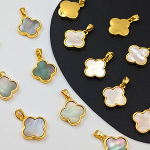 May include: A collection of 14 gold clover charms with a variety of iridescent mother of pearl inlay. The charms are arranged on a black and white background.