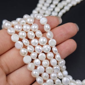 Könnte beinhalten: Eine Strähne weißer Süßwasserperlen. Die Perlen sind rund und haben eine glatte, glänzende Oberfläche. Die Perlen sind auf einem durchsichtigen Faden aufgefädelt und haben einen Durchmesser von etwa 8 mm.