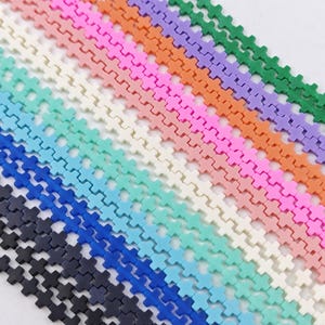 May include: A variety of cross-shaped beads in different colors, including black, blue, light blue, turquoise, white, pink, orange, purple, and green. The beads are arranged in rows, creating a colorful and textured pattern.