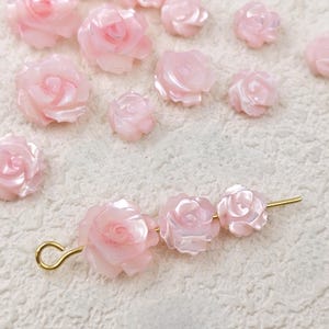 May include: A collection of pink shell rose flower embellishments, some are strung on a gold wire.