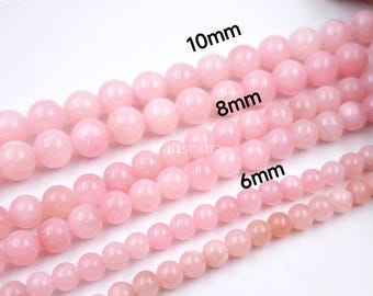 Puede incluir: Tres hileras de cuentas redondas y lisas de color rosa claro. La fila superior está etiquetada como 10mm, la fila central como 8mm y la fila inferior como 6mm. Cada hilera consta de cuentas esféricas, pulidas y uniformes en tono rosa.