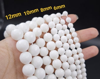 Peut inclure: Perles rondes blanches de différentes tailles, 6 mm, 8 mm, 10 mm et 12 mm, disposées en rangées sur une main.