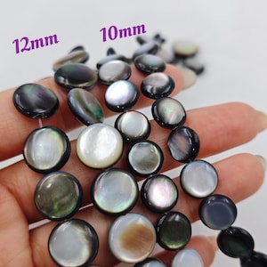 Op de afbeelding: Een streng zwarte en witte schelp kralen, met sommige kralen die 12 mm meten en andere 10 mm.