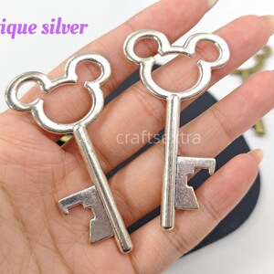 May include: Two antique silver metal keys featuring a circular head with two smaller circular ears, resembling a mouse silhouette. The keys have a straight shaft and a notched bit at the bottom. The text antique silver is visible in the image.