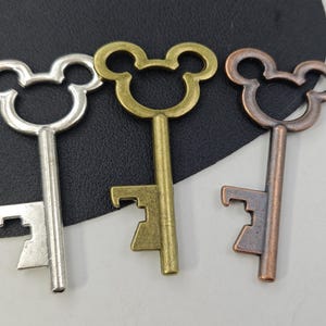 Könnte beinhalten: Drei antike Schlüsselanhänger mit Mickey-Maus-Kopf-Design. Die Schlüssel sind silber, gold und kupferfarben.