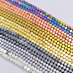Puede incluir: Primer plano de una variedad de cuentas hexagonales en diferentes colores metálicos, incluyendo plata, oro, cobre e iridiscente.