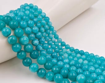Peut inclure: Un collier de perles rondes et polies de couleur turquoise avec un léger marbrage blanc. Les perles varient en taille, disposées en dégradé du plus grand au plus petit. Le texte CRAFTSEXTRA est visible au centre de l'arrangement.
