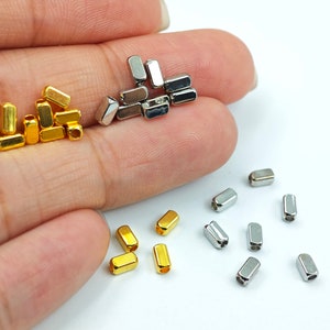May include: A close-up of two piles of metal barrel-shaped beads. One pile is gold and the other is silver. The beads are small and have a hole in the centre.