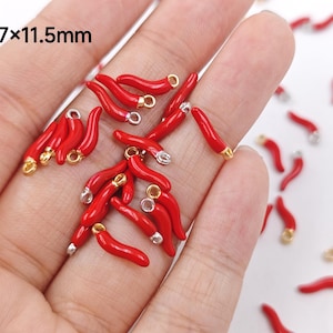 Puede incluir: Primer plano de una mano sosteniendo una variedad de dijes de chile rojo con detalles dorados y plateados. Los dijes miden aproximadamente 3,7 x 11,5 mm.