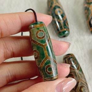 Puede incluir: Un conjunto de cinco cuentas de ágata verde y marrón con un patrón geométrico. Las cuentas están enhebradas en un cordón negro.