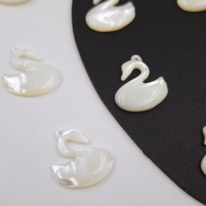 May include: A collection of white mother of pearl swan charms. The swans are all facing the right and have a delicate, elegant design.