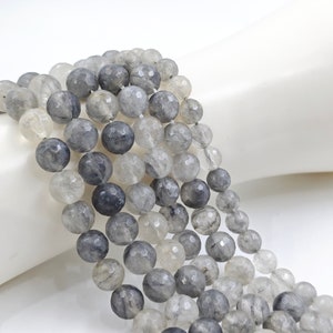 May include: Multiple strands of faceted, round beads in shades of grey and clear. The beads are strung together, creating a layered effect. The beads have a polished, reflective surface, and are likely made of a gemstone or crystal.