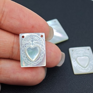 Può includere: Tre ciondoli rettangolari in madreperla bianca con un designo intagliato a forma di cuore e croce.