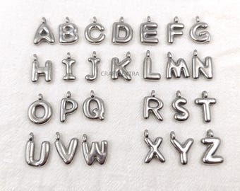 May include: A collection of silver-toned metal alphabet letter charms, each featuring a small loop at the top for attachment. The letters are arranged in alphabetical order from A to Z, displaying a smooth, rounded, and polished surface finish.