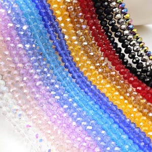 May include: Assortment of crystal beads in various colors, including clear, light pink, blue, yellow, red, and black. The beads are faceted and have a shiny, iridescent finish.