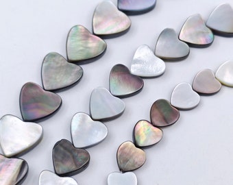 May include: A strand of heart-shaped shell beads in shades of white and iridescent black. The beads are strung together on a clear thread.