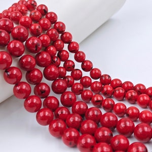 May include: A strand of red gemstone beads with black marbling. The beads are round and smooth, and they are strung on a clear thread.