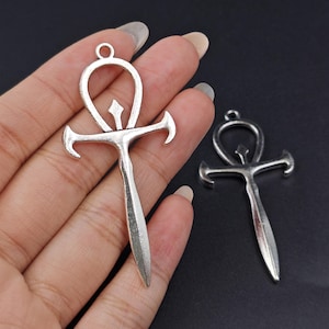 May include: Two silver Ankh pendants with a detailed design. The pendants are on a black background.