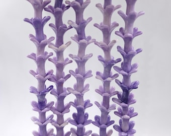 May include: Close-up of several stems of lavender-colored artificial flowers. The flowers have a layered, textured appearance with a gradient of purple hues. The stems are arranged vertically against a white background.
