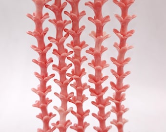 May include: Rows of coral-like structures in a soft coral pink hue. Each structure has a central stem with multiple branching elements, creating a repeating pattern. The background is a plain white, highlighting the intricate details of the objects.