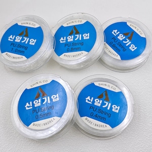 Puede incluir: Cinco carretes de cuerda elástica transparente, cada uno etiquetado con "Shin Il Co. 신일기업 PU.String" con un grosor diferente en milímetros: 1,0 mm, 0,8 mm, 0,6 mm, 0,5 mm y 0,4 mm.