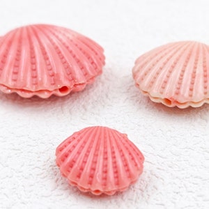 K&ouml;nnte beinhalten: Drei rosa Muscheln in verschiedenen Gr&ouml;&szlig;en. Die gr&ouml;&szlig;te Muschel befindet sich oben links, die mittelgro&szlig;e Muschel oben rechts und die kleinste Muschel unten in der Mitte.