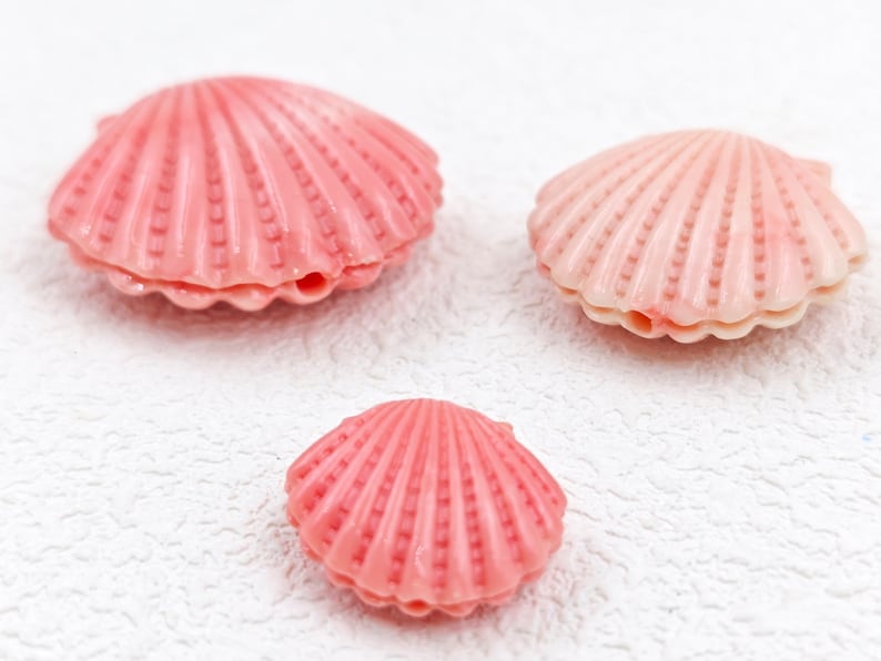 K&ouml;nnte beinhalten: Drei rosa Muscheln in verschiedenen Gr&ouml;&szlig;en. Die gr&ouml;&szlig;te Muschel befindet sich oben links, die mittelgro&szlig;e Muschel oben rechts und die kleinste Muschel unten in der Mitte.