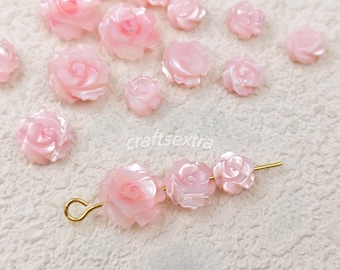 Puede incluir: Una colección de cuentas con forma de rosa de color rosa pálido esparcidas alrededor de un alfiler de metal dorado que presenta tres cuentas de rosa idénticas unidas en fila. El texto craftsextra es visible en el centro de la imagen.