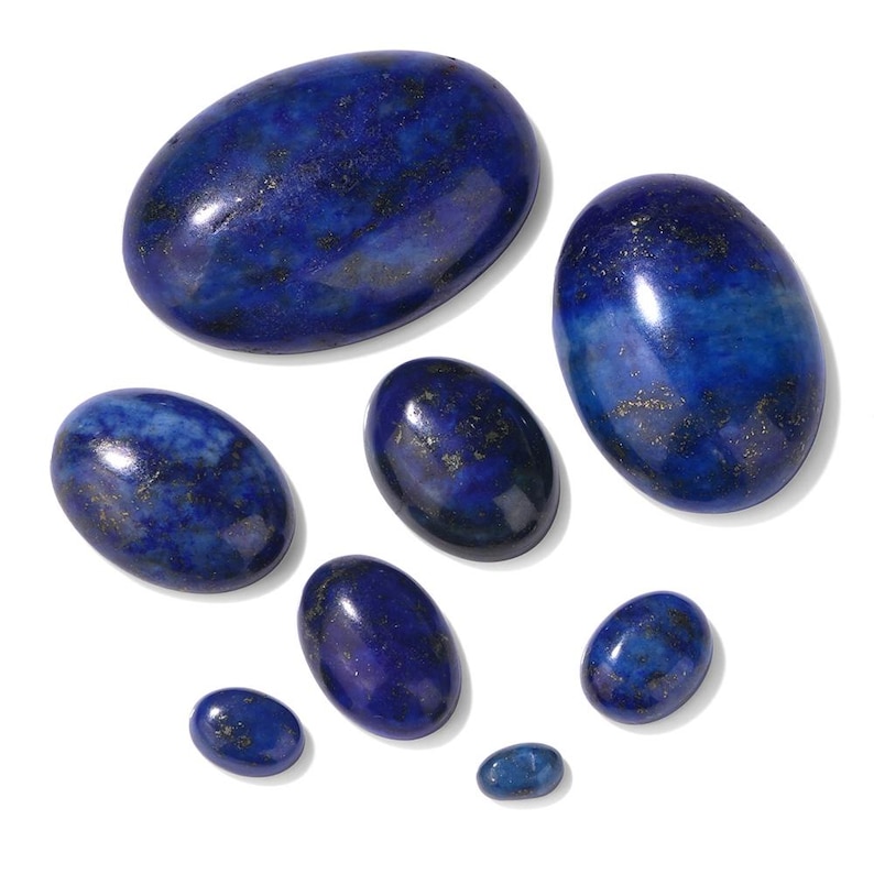 K&ouml;nnte beinhalten: Eine Sammlung ovaler Lapis-Lazuli-Edelsteine in verschiedenen Gr&ouml;&szlig;en. Die tiefblauen Steine mit Goldeinschl&uuml;ssen haben eine polierte Oberfl&auml;che und sind vor einem wei&szlig;en Hintergrund angeordnet. Diese Edelsteine eignen sich f&uuml;r die Schmuckherstellung.