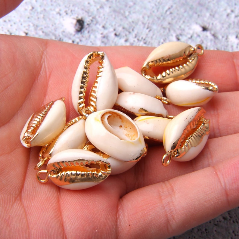 Puede incluir: Una colecci&oacute;n de conchas blancas con detalles dorados. Las conchas tienen un acabado liso y pulido y est&aacute;n enhebradas con alambre dorado.