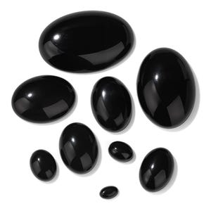 K&ouml;nnte beinhalten: Eine Sammlung polierter, oval geformter, schwarzer Edelsteine in verschiedenen Gr&ouml;&szlig;en. Die Steine haben eine gl&auml;nzende, reflektierende Oberfl&auml;che und sind vor einem wei&szlig;en Hintergrund angeordnet. Die Edelsteine sind wahrscheinlich f&uuml;r Schmuck oder Dekorationszwecke bestimmt.