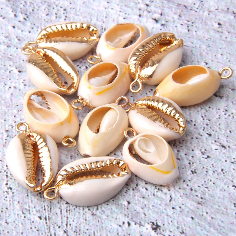 Puede incluir: Una colecci&oacute;n de 10 conchas de cauri blancas con detalles dorados. Cada concha tiene un lazo dorado adjunto para la elaboraci&oacute;n de joyas.