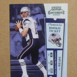 May include: A 2000 Playoff Contenders football card featuring Tom Brady in a New England Patriots uniform. The card includes a "Championship Rookie Ticket" design and Brady's name and team information.