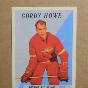 Peut inclure: Une carte de hockey vintage représentant Gordie Howe, un joueur des Red Wings de Detroit. La carte a un fond bleu et blanc avec une image rouge et blanche de Howe dans son uniforme de hockey. Le texte "GORDY HOWE" est imprimé en noir en haut de la carte, et "DETROIT RED WINGS WING" est imprimé en noir en bas.