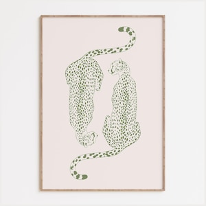 May include: A framed wall art print featuring two stylized cheetahs in a muted olive green line drawing style. The cheetahs are positioned vertically against a pale blush pink background, with one facing downward and the other facing upward.