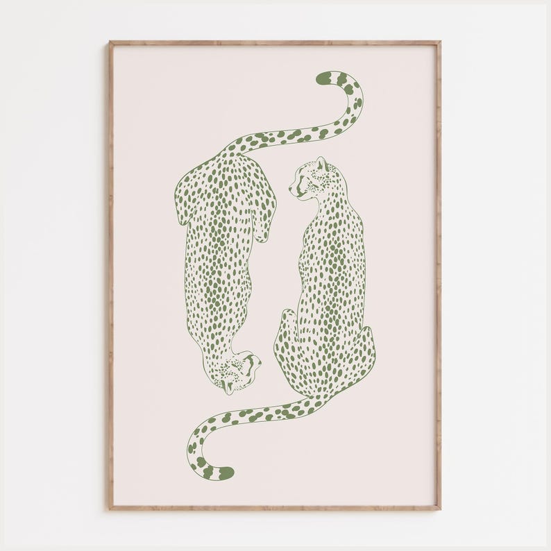 May include: A framed wall art print featuring two stylized cheetahs in a muted olive green line drawing style. The cheetahs are positioned vertically against a pale blush pink background, with one facing downward and the other facing upward.