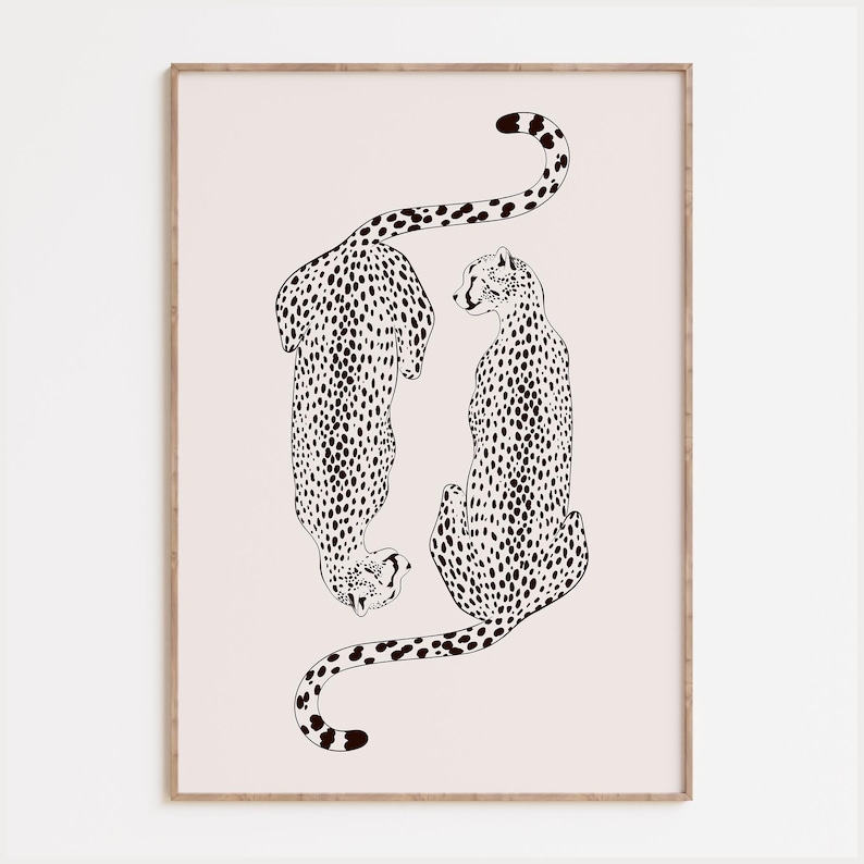May include: A framed wall art print featuring a black line drawing of two cheetahs on a pale pink background. One cheetah is positioned facing downward while the other faces upward, both covered in black spots, enclosed in a light wood frame.