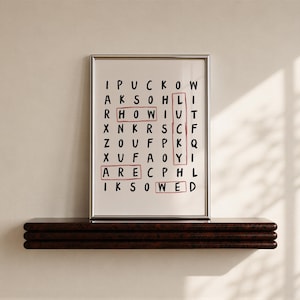 May include: A framed wall art print featuring a word search puzzle on a white background with black letters. The words HOW, LUCKY, ARE, and WED are highlighted with red rectangular outlines. The print is enclosed in a thin silver metal frame.