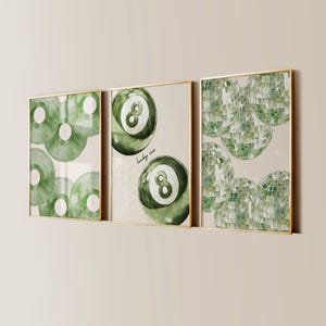 May include: Three framed art prints with gold frames. The prints feature watercolor designs of green vinyl records, an eight ball, and disco balls. The middle print has the text "lucky me". The background is a neutral beige color.