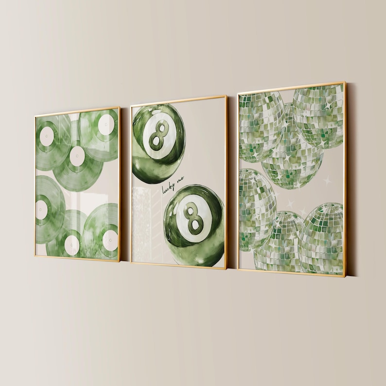May include: Three framed art prints with gold frames. The prints feature watercolor designs of green vinyl records, an eight ball, and disco balls. The middle print has the text "lucky me". The background is a neutral beige color.
