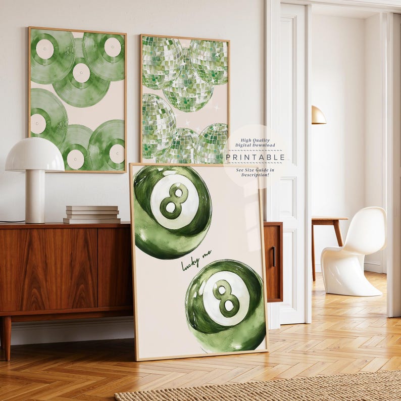 May include: Three framed art prints with a light beige background. The prints feature green watercolor designs of vinyl records, disco balls, and an eight ball with the text "lucky me". The prints are in wooden frames.