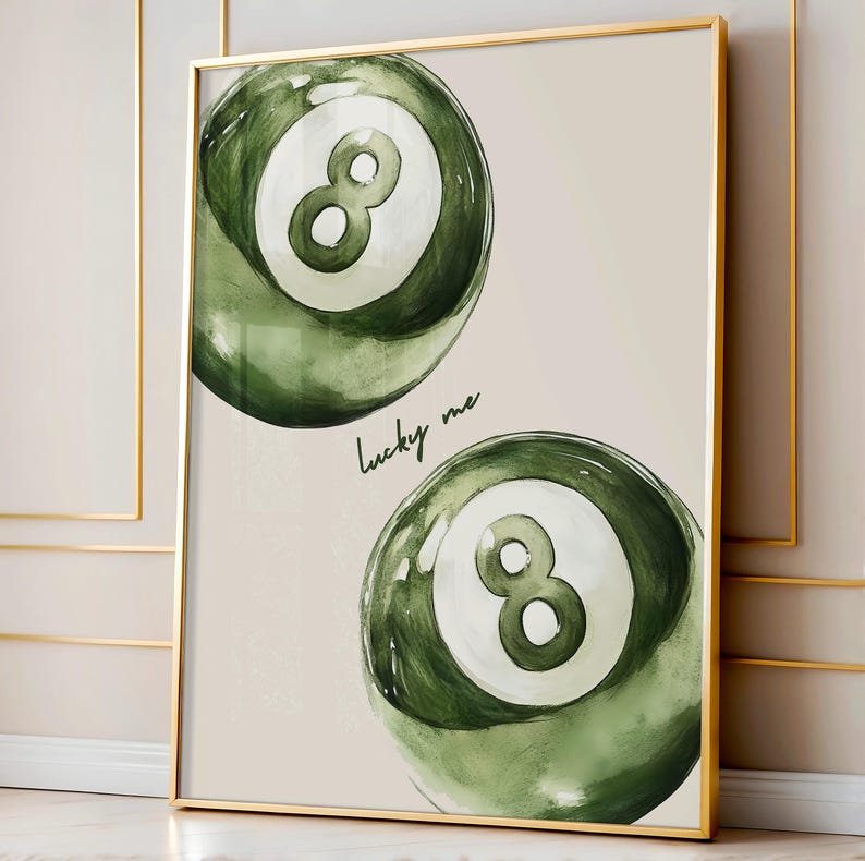 May include: A framed print featuring two green and white eight-ball pool balls. The balls have a watercolor effect and are set against a neutral background. The words "lucky me" are written in cursive below the top ball.