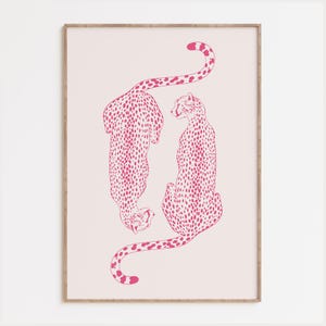 May include: A framed wall art print featuring two cheetahs illustrated in a vibrant hot pink color against a pale blush pink background. The cheetahs are positioned vertically, one facing downward and one facing upward, with detailed spots.