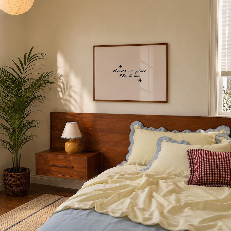 Pu&ograve; includere: Una stampa artistica incorniciata con il testo "there's no place like home" e due piccole icone a forma di stella. La stampa &egrave; esposta sopra una testiera in legno con un set da letto giallo con bordi smerlati blu e un cuscino a quadretti rossi.