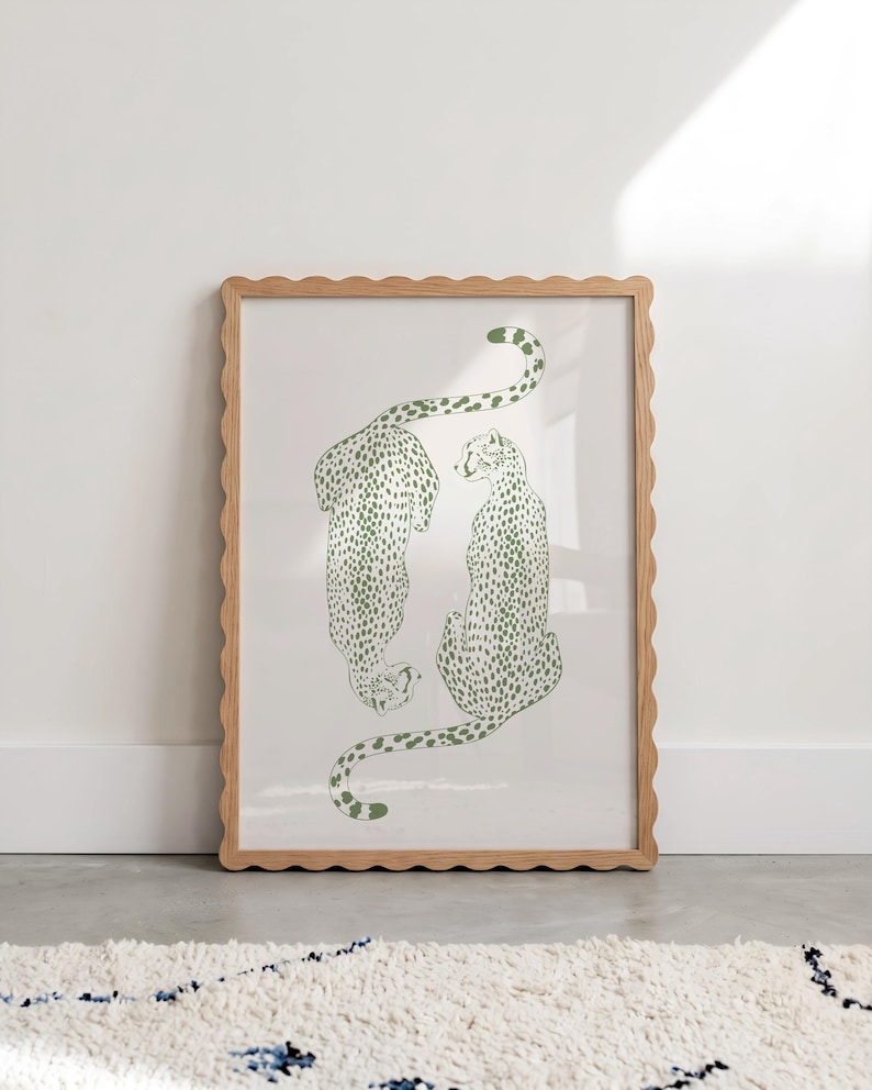 May include: A framed wall art print featuring two green cheetahs with spotted patterns on a white background. The cheetahs are positioned in a mirrored orientation, one facing downward and one sitting upright. The frame has a light wood scalloped edge.