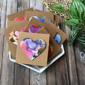 May include: A stack of brown cardstock cards with colorful heart-shaped paper embellishments. The hearts have a marbled design with gold accents.