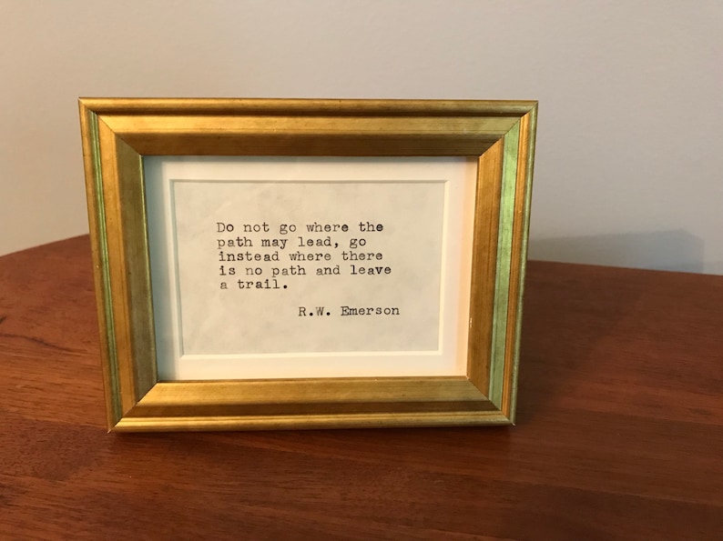 May include: A framed print with a gold frame and a white background. The print features a quote by R.W. Emerson: "Do not go where the path may lead, go instead where there is no path and leave a trail."