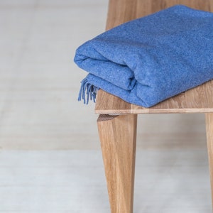 以下が含まれることがあります： 4本の脚が付いた木製のベンチの上に、青い毛布が折り畳まれています。ベンチは明るい茶色の木でできています。